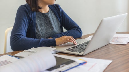Woman typing on laptop surrounded by papers