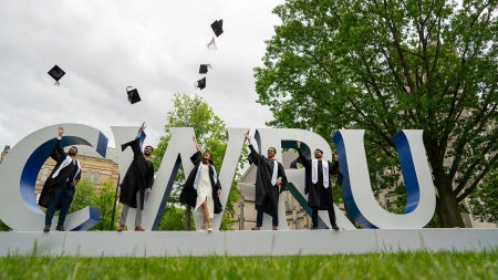 Five students stand in front of the CWRU sign and throw their commencement hats in the air
