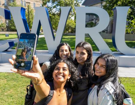 A group of students take a selfie near the big CWRU letters on the first day of classes.