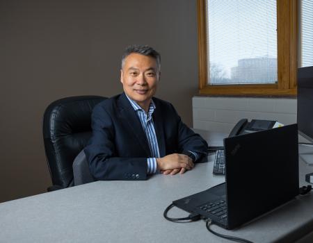 Photo of person sitting at desk with computers, smiling at camera