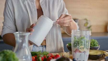 Close up photo of a woman adding protein powder to a smoothie