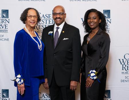 Three dental alumni award dinners pose in front of Case Western Reserve School of Dental Medicine logos after receiving their honors.