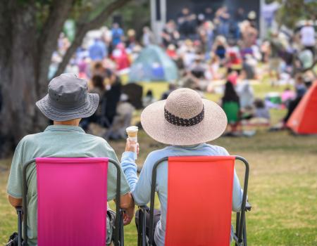 Photo of an elderly couple sitting next to one another in lawn chairs at an outdoor event