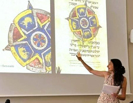 Photo of Elina Gertsman presenting at a symposium with the cover of her book on abstraction in medieval art projecting on the wall