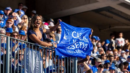 Excited member of the CWRU community holds a CWRU flag at a football game during Homecoming and Reunion weekend. 