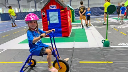 Photo of a child wearing a helmet riding a tricycle on a model town set up for CWRU's Safety Town