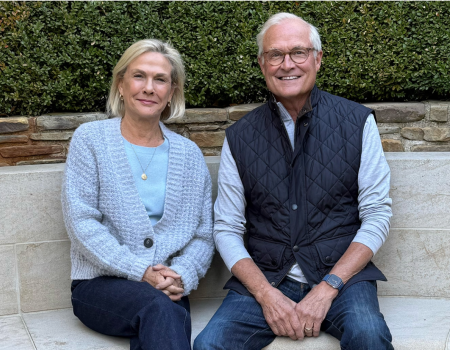 Lady in a blue sweater sitting next to a man with a vest outside 