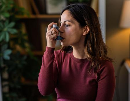 Photo of a woman sitting in her home using an inhaler
