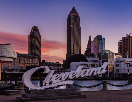 Photo of the Cleveland script sign in front of the Rock and Roll Hall of Fame with the city skyline in the background at dusk