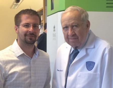 Two men standing side by side, one on left wearing dress shirt and on right white lab coat