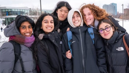 A group of six students bundled up in winter coats on campus.