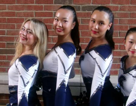 Four members of the CWRU Dance Team pose in their uniforms in front of a brick wall.