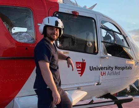 CRNA student Robert Sharkey stands in front of a medical helicopter on a rooftop.