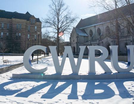 Photo of the CWRU letters on a snowy day with Adelbert Hall and Amasa Stone Chapel behind them