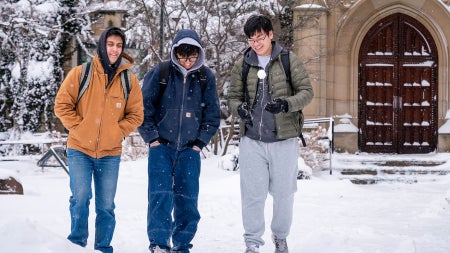 Photo of three students walking across Mather Quad on a snowy day