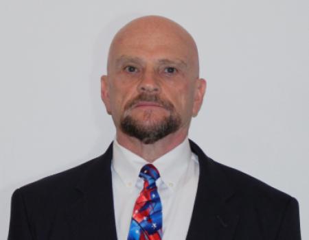 Denver Jenkins, DDS poses in front of a plain backdrop in a black suit with red and blue tie.