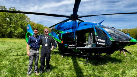 Tanner Purnhagen stands in front of a blue helicopter in a field.