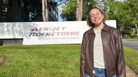 Photo of Andrea Silva posing for a photo in front of the Aerojet Rocketdyne sign during an internship