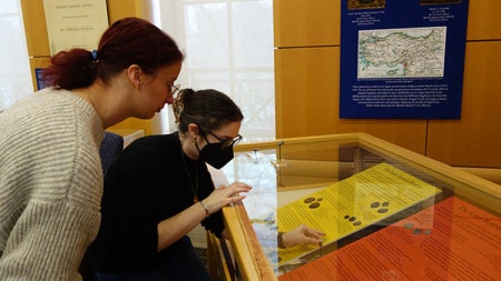Two students assemble the ancient small coins in a glass exhibit case at Kelvin Smith Library