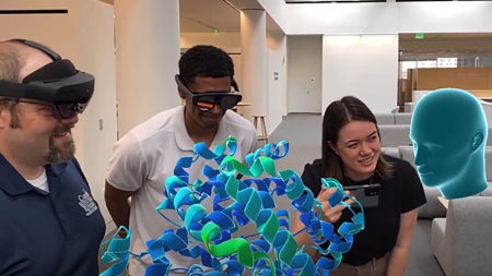 Group wearing extended reality headsets gather around an illustration of molecules 