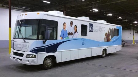 The white and blue CWRU dental clinic bus sits in a garage.