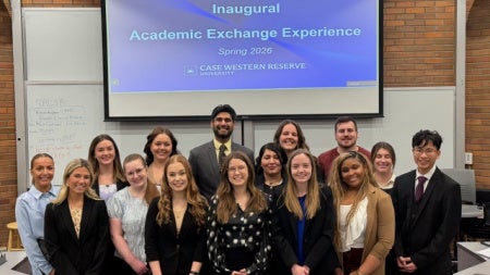 Group of students standing in front of a screen that says "Inaugural Academic Exchange Experience Spring 2026"