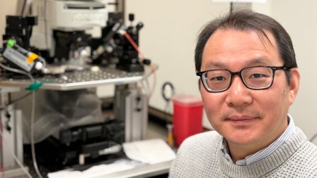 A scientist sits next to a patch clamp electrophysiology setup