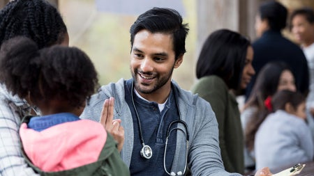 Photo of a doctor smiling while talking to a mom and her young child in a health clinic