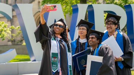 Four graduates in their caps and gowns posed for a selfie in front of the CWRU letters