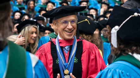 A smiling person in academic regalia and a cap stands amidst a group of graduates wearing blue gowns and caps, conveying a joyful, celebratory atmosphere.