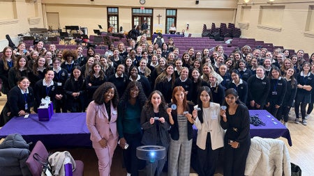 Photo of the Women in Business executive board posing for a photo with students from Saint Joseph Academy in the background