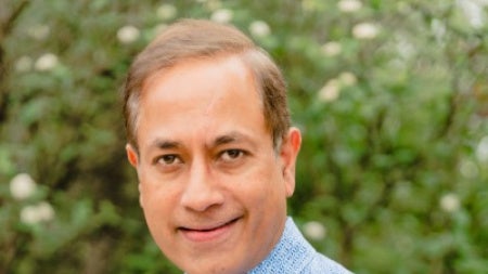 Manish Valiathan wearing a blue shirt with a tree in the background 