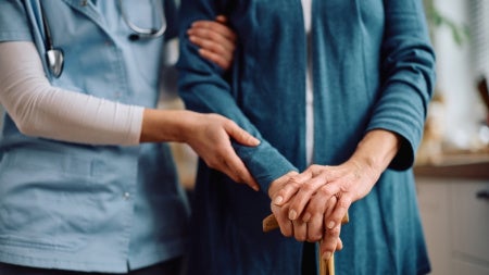 Close up of nurse and senior woman with walking cane during home visit. 