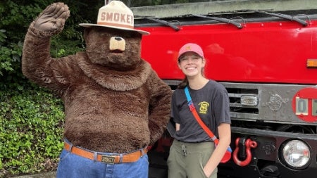Meg Corley standing with Smokey the bear in front of a truck