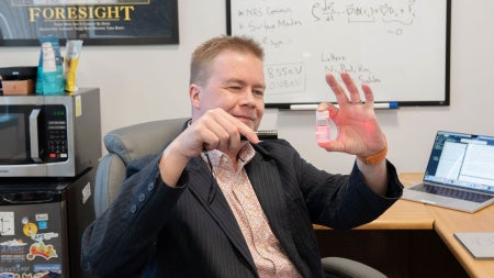 A scientist directs a laser beam through a clear plastic container filled with silica nanoparticles. 