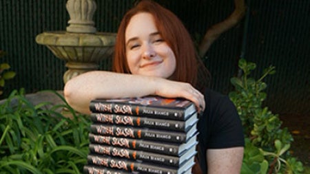 Julia Bianco sitting in the grass with a stack of her new books in her lap