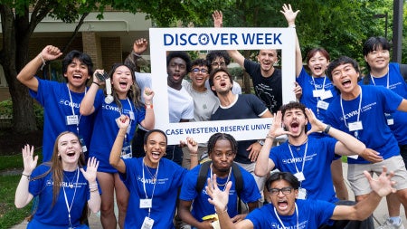 A large group of orientation leaders and student move-in volunteers gather for a photo during move-in weekend posing with a photo frame that says "Discover Week Case Western Reserve University"