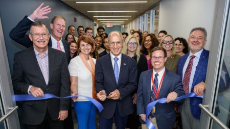 Dean Gerson cutting a blue ribbon surrounded by School of Medicine staff and faculty