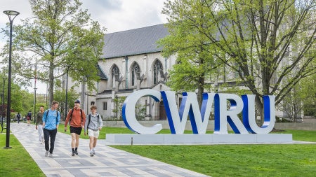 Three CWRU students walk down the Binary Walkway with the CWRU letters behind them
