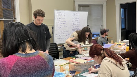 Students sitting and standing around a table working on building books