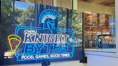 Illuminated neon sign that says "Knight Bytes" and "Food, Games, Good Times" hanging in Leutner Commons