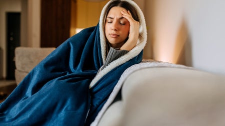 Photo of woman wrapped in a blanket on couch, head in hand.