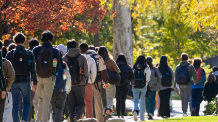 A line of students walk on the CWRU campus with a color-changing trees in the background. 