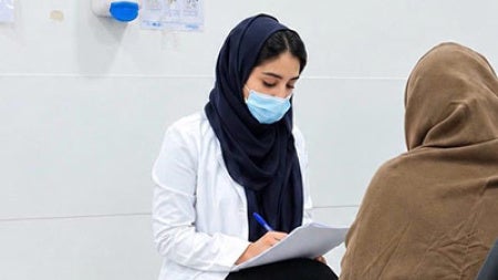 Rania Aljohani speaks with a patient and takes notes with the patient's back to the camera
