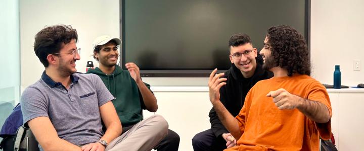 four medical students sitting in chairs, laughing with each other as they act out an improv sketch
