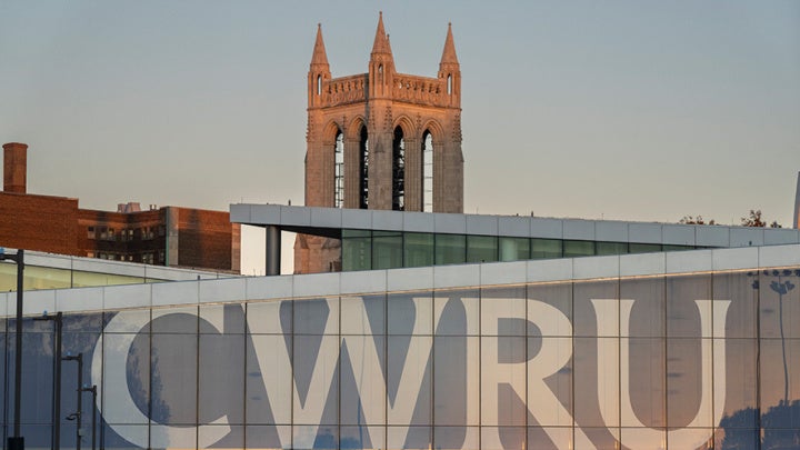 Photo of the CWRU letters covering the windows in Tinkham Veale University Center with the Church of the Covenant bell tower in the background