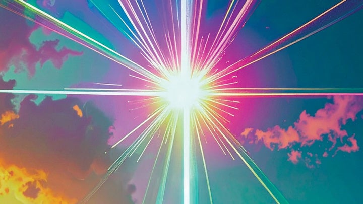 A colorful starburst pattern with multicolored beams emanating from a bright white center against a cloud-filled background.