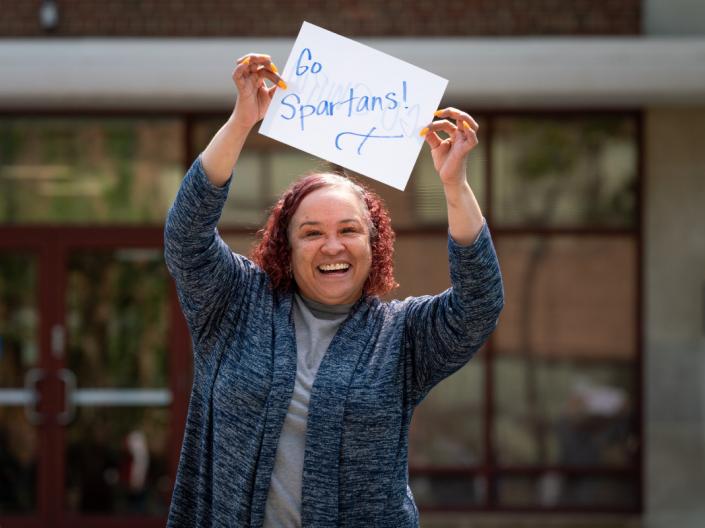 A woman smiling while holding a sign that reads "Go Spartans!"