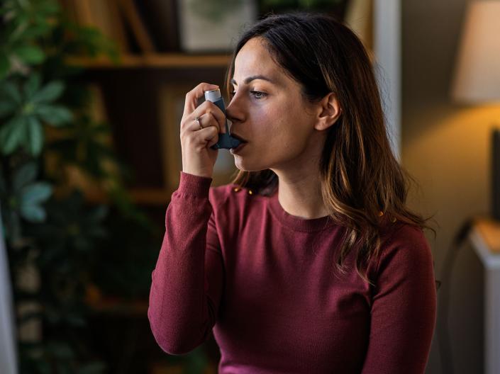 Photo of a woman sitting in her home using an inhaler
