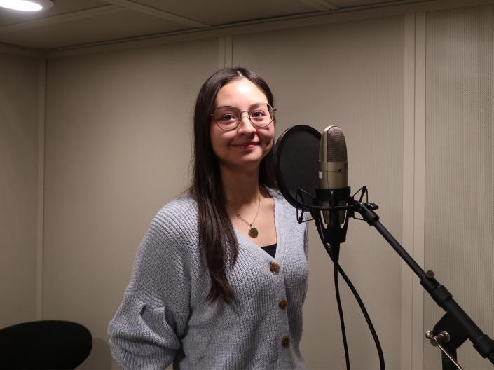 A woman stands next to a microphone in a double-walled, sound-isolated booth